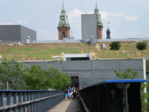 A raised walkway into a shopping center. The roof of the mall is covered in grass and trees.